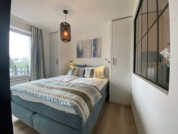A bedroom with a large bed, a window with curtains, a hanging light fixture, and artwork on the wall. - Ferienwohnung Schöne Aussicht (Winterberg)