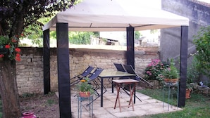Une terrasse couverte, dotée d’une table et de chaises, entourée de murs en pierre et agrémentée de plantes en pot.