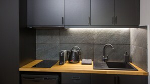 Una cocina moderna con armarios oscuros, encimera de madera, hervidor, cafetera y un fregadero.