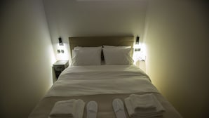 Una cama bien hecha con almohadas, una mesita de noche y un par de pantuflas sobre la cama.