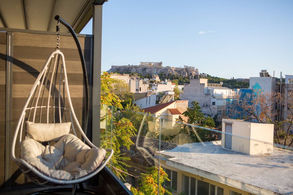 A hanging chair with a cushion, a view of a cityscape with a prominent building on a hill, and a clear sky.