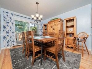 Ein Essbereich mit einem Holztisch, Stühlen, einer Chandelüster und einem Schrank mit Flaschen.