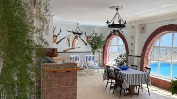 A spacious dining area with a high ceiling, a stone fireplace, and a view of the sea through large windows.