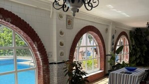 A sunlit room with a pool view, arched windows, a chandelier, and striped lounge chairs.