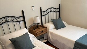 Two single beds with headboards, a bedside table with a lamp, and a wicker basket.