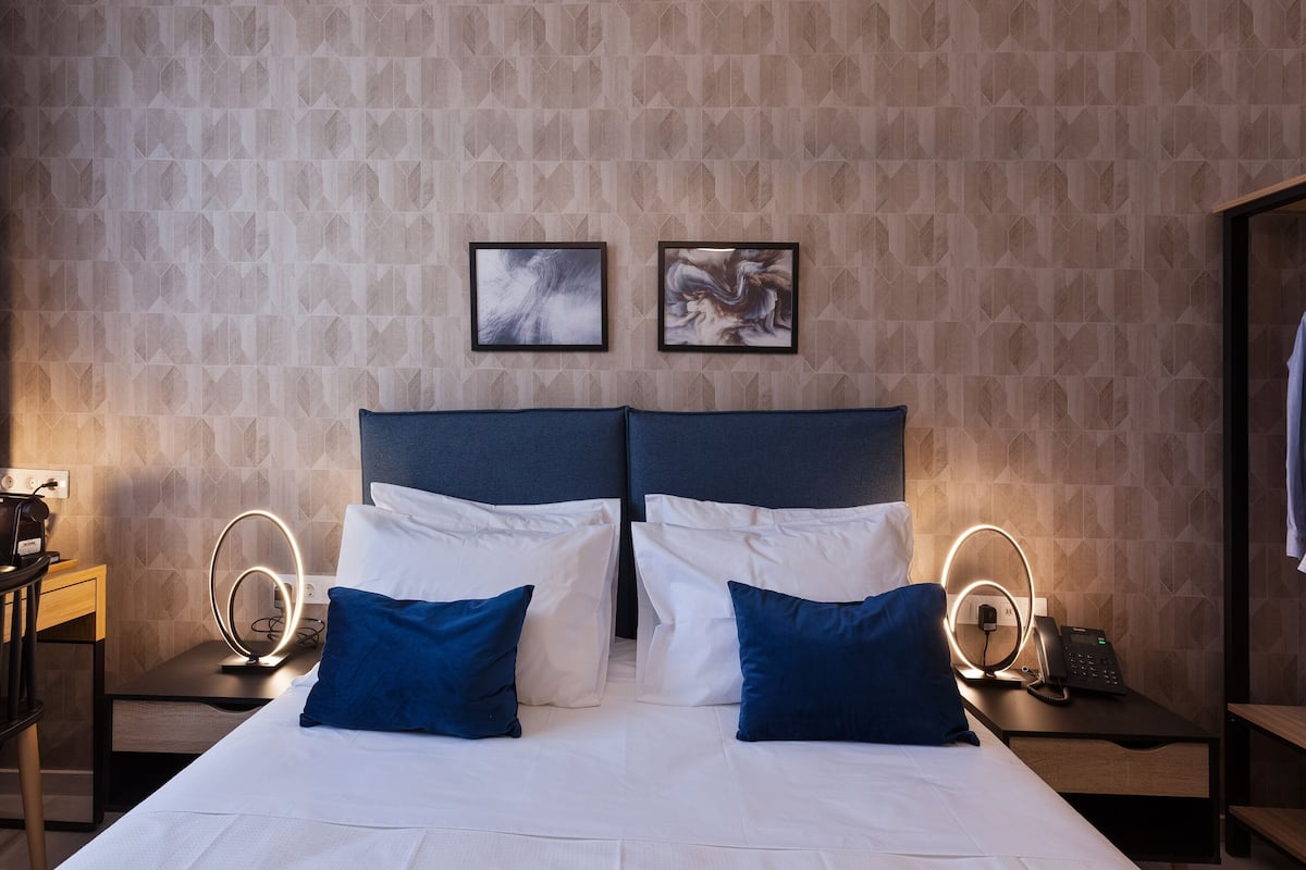 Hotellihuone, jossa on suuri sänky, kaksi yöpöytää valaisimineen, työpöytä ja kaksi kehystettyä kuvaa seinällä.