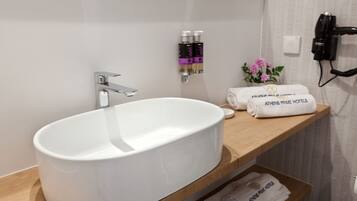 A modern bathroom with a large white sink, a wooden vanity, and toiletries on the wall.