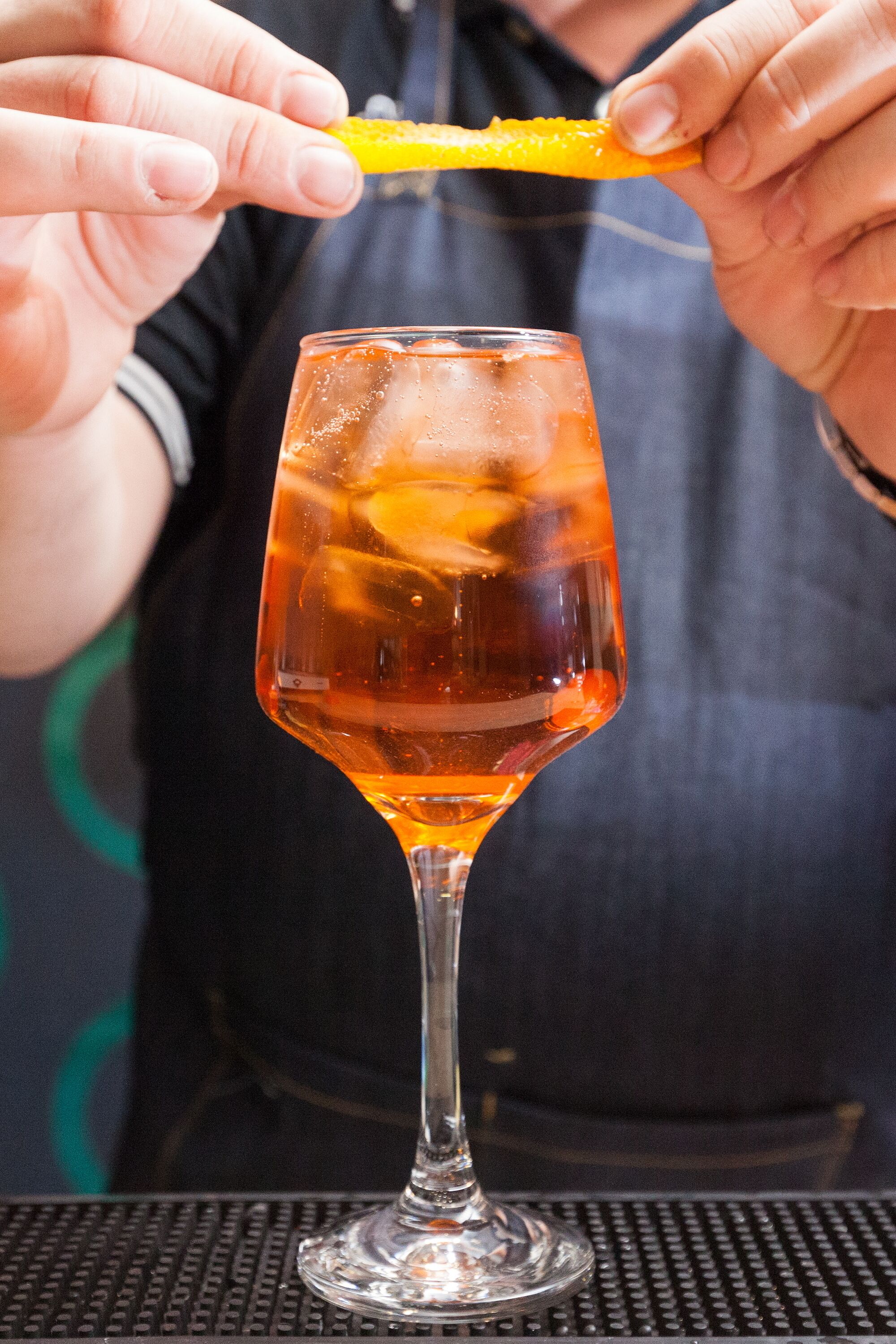 A person holding a lemon wedge above a glass with ice cubes.