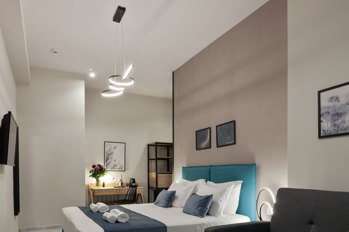 Moderni hotellihuone, jossa on sänky, sohva, työpöytä ja pieni pöytä, jonka päällä on omenoita.