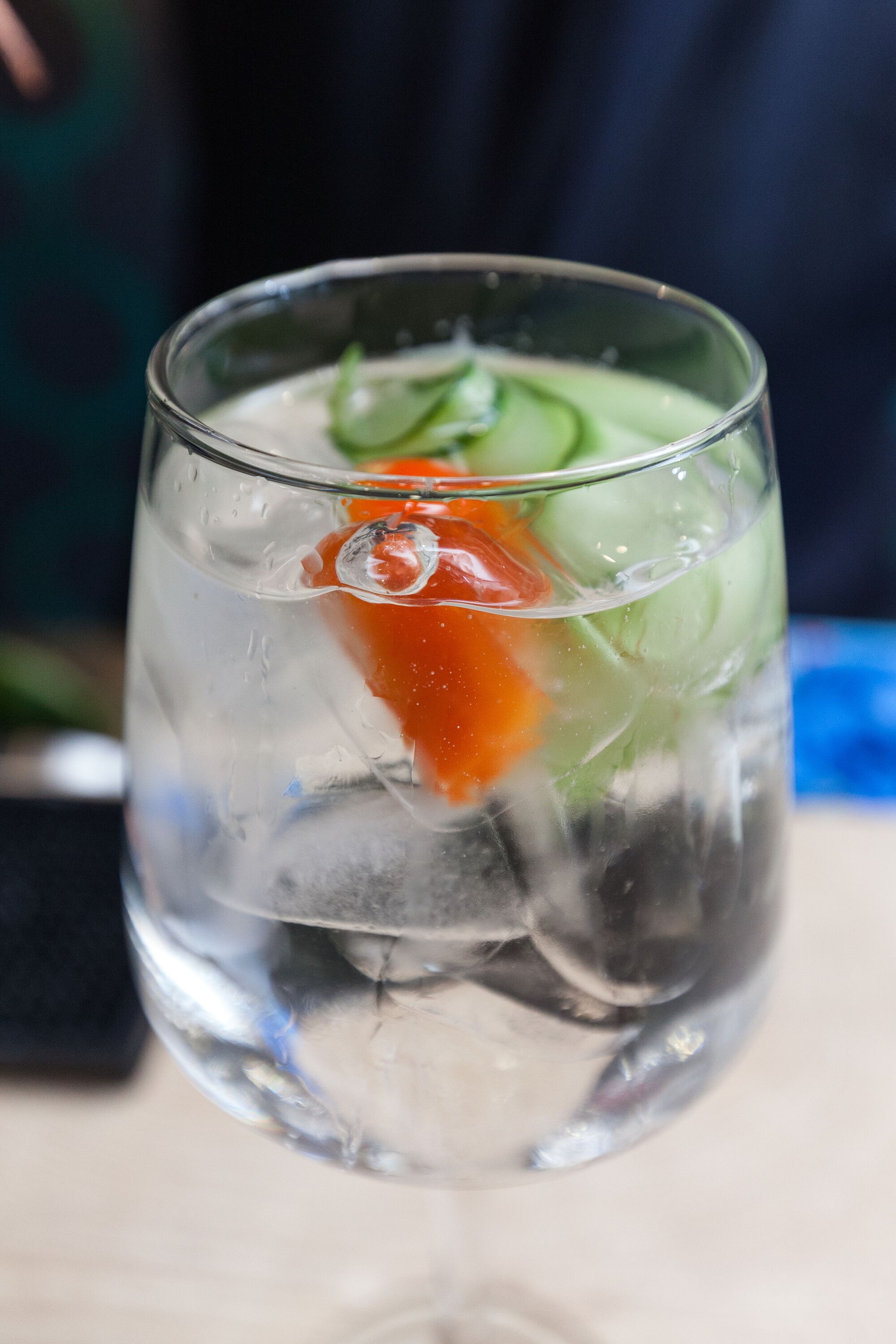 Ein klares Glas mit Eiswürfeln, einer Orangenscheibe und grüner Dekoration.
