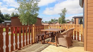 Eine Holzterrasse mit Tisch und Korbstühlen, umgeben von einem Holzzaun.