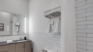 A modern bathroom with white tiles, a sink, cabinets, a toilet, and a shower area. - Bardo Loft Suite #201 (Dallas)