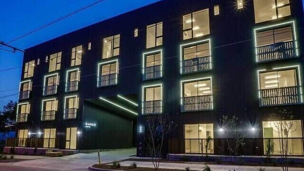 A modern multi-story building with illuminated windows and balconies, a visible entrance, and a sign that reads "BARDO." - Bardo Loft Suite #201 (Dallas)