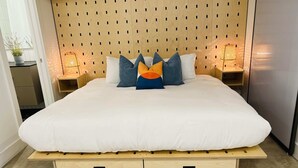 Een moderne slaapkamer met een houten hoofdbord, een groot bed met wit beddengoed en twee nachtkastjes met lampen.