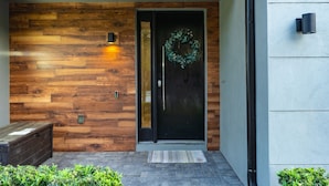 A modern building entrance with a wooden wall, a black door with a wreath, and a bench outside. - Disney-Themed Escape – Frozen & Star Wars Rooms, Pool, Games & Family Fun (Kissimmee)