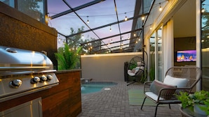 An outdoor patio with a grill, a small pool, a chair, and a TV screen. - Disney-Themed Escape – Frozen & Star Wars Rooms, Pool, Games & Family Fun (Kissimmee)