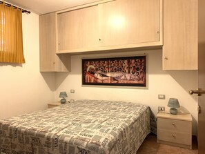 A bedroom with a bed, a nightstand, a lamp, a painting, and a wardrobe.