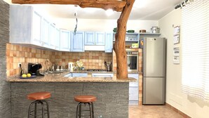 Una cocina con una isla central, dos taburetes, un refrigerador y una viga de techo de madera.