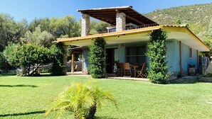 Una casa con chimenea de piedra, un porche cubierto y un jardín pequeño.