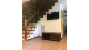 A spacious living area with a wooden staircase, a flat-screen TV mounted on the wall, and a wooden entertainment unit. - Heart and soul on Windrock (Oliver Springs)