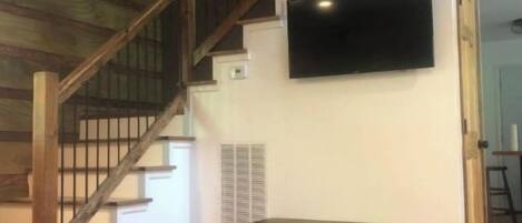 Ampla sala de estar com escada de madeira, TV de tela plana na parede e móvel de entretenimento em madeira.