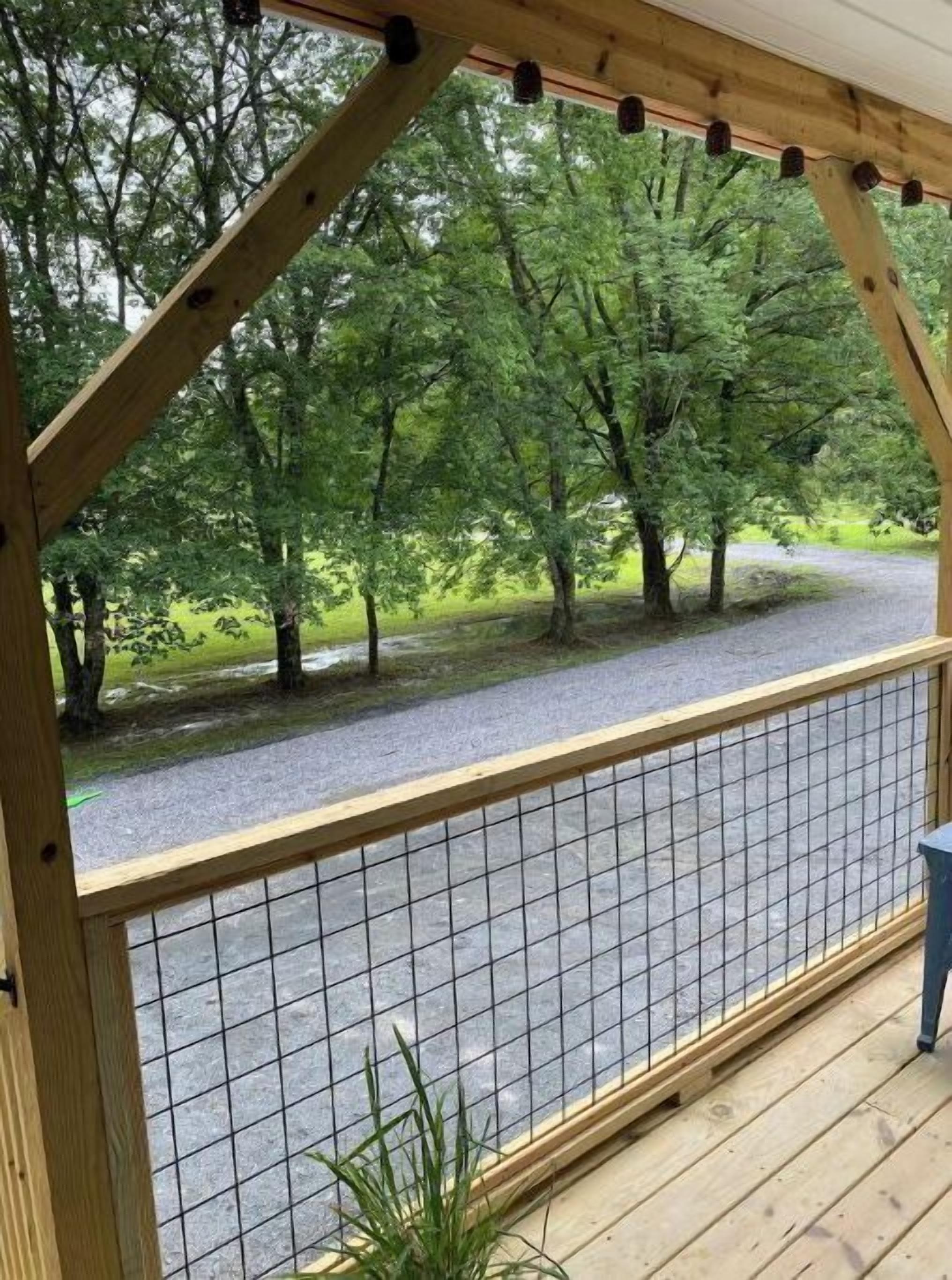 Eine Holzdielen-Terrasse mit Metallzaun, die auf einen Schotterweg und Bäume blickt.