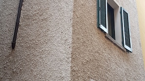A building facade with a textured wall, a sign reading "vicolo Paradiso," and a door with a window above it. - The little house (Domaso)