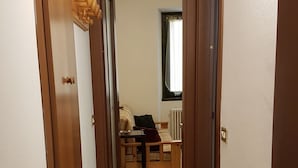 A hallway leading to a bedroom with a bed, a nightstand, and a window with blinds. - The little house (Domaso)