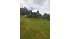 A wooden house with a porch, surrounded by a grassy field and trees. - Comfort chalet in the heart of Auvergne  (Maurines)