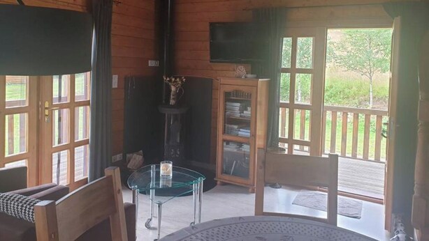 A cozy cabin interior with wooden walls, a glass table, a bookshelf, and a television. - Comfort chalet in the heart of Auvergne  (Maurines)