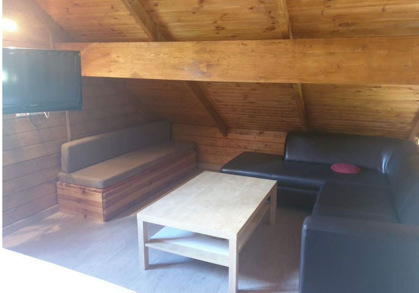 A cozy attic room with a wooden ceiling, a sofa, a black leather chair, and a small table.