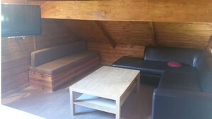 A cozy attic room with a wooden ceiling, a sofa, a black leather chair, and a small table. - Comfort chalet in the heart of Auvergne  (Maurines)