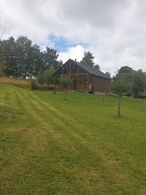 A wooden house with a porch, surrounded by a grassy field and trees.