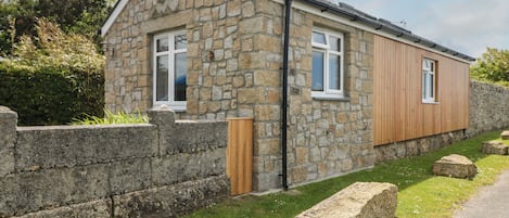 A stone house with a wooden extension, a stone wall, and a grassy yard.