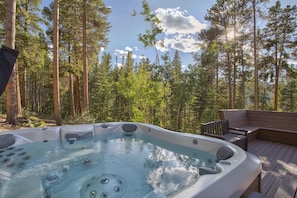 Relax in a serene forest setting, surrounded by tall pine trees, with a hot tub and comfortable seating options.
