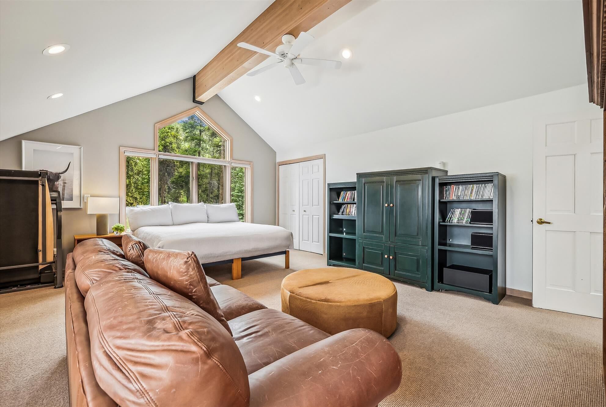 Une chambre spacieuse avec un grand lit, un canapé en cuir, un pouf rond, un ventilateur de plafond et des étagères intégrées.