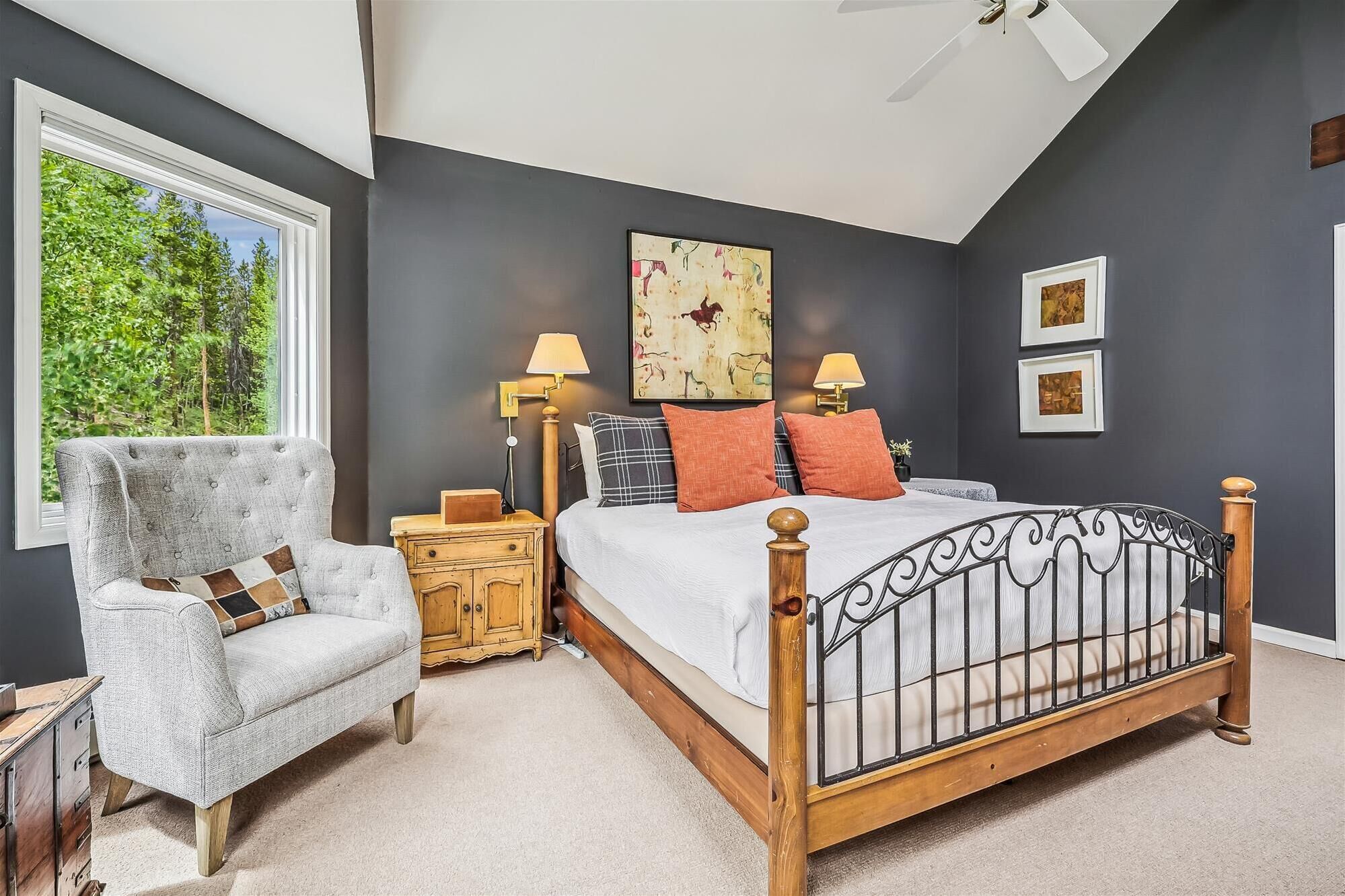 A bedroom with a bed, a chair, a nightstand, a ceiling fan, and artwork on the walls.