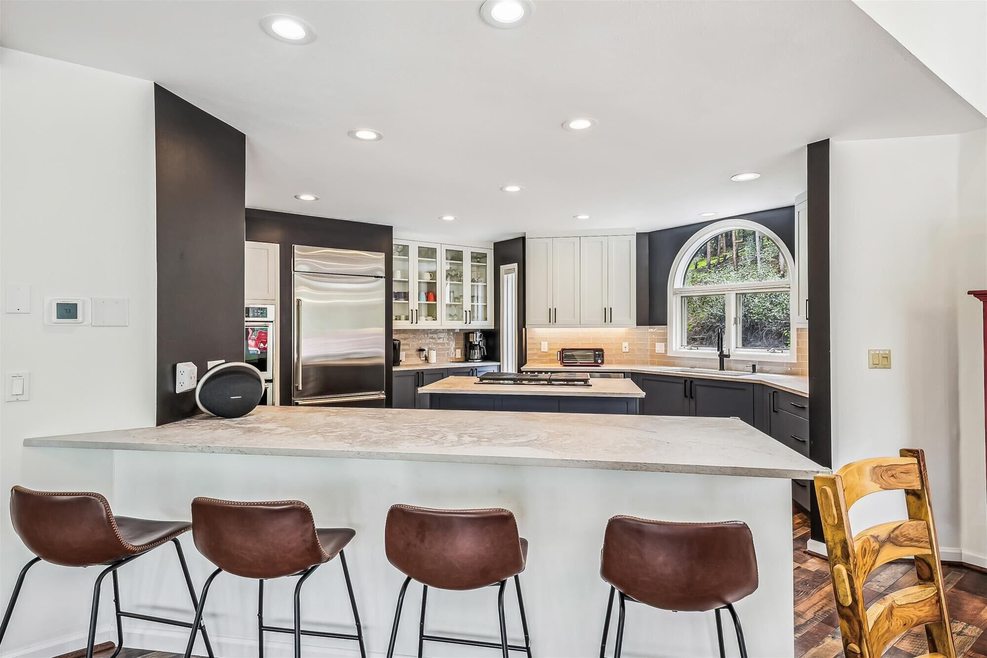 A modern kitchen with a central island, bar stools, and a large window.