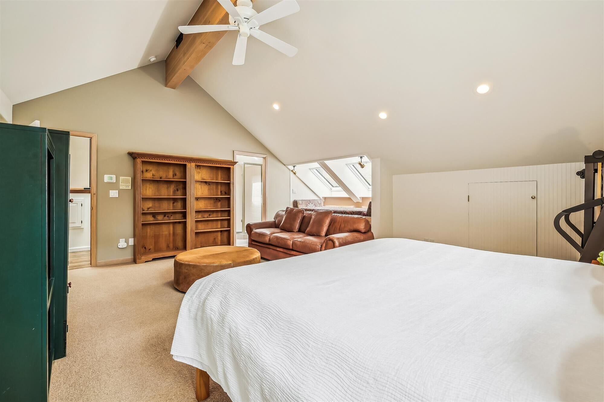 A bedroom with a large bed, a wooden wardrobe, a brown leather sofa, and a ceiling fan.