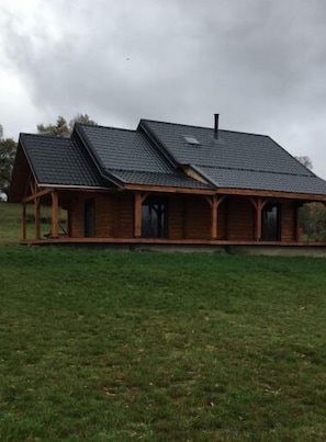 A wooden cabin with a sloped roof and a chimney, surrounded by a grassy field.