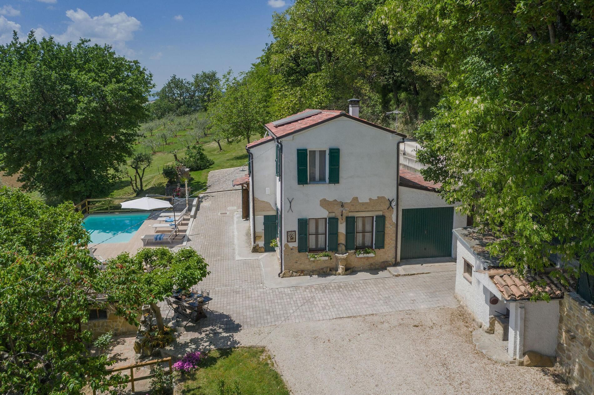 A two-story house with a swimming pool, surrounded by lush greenery.