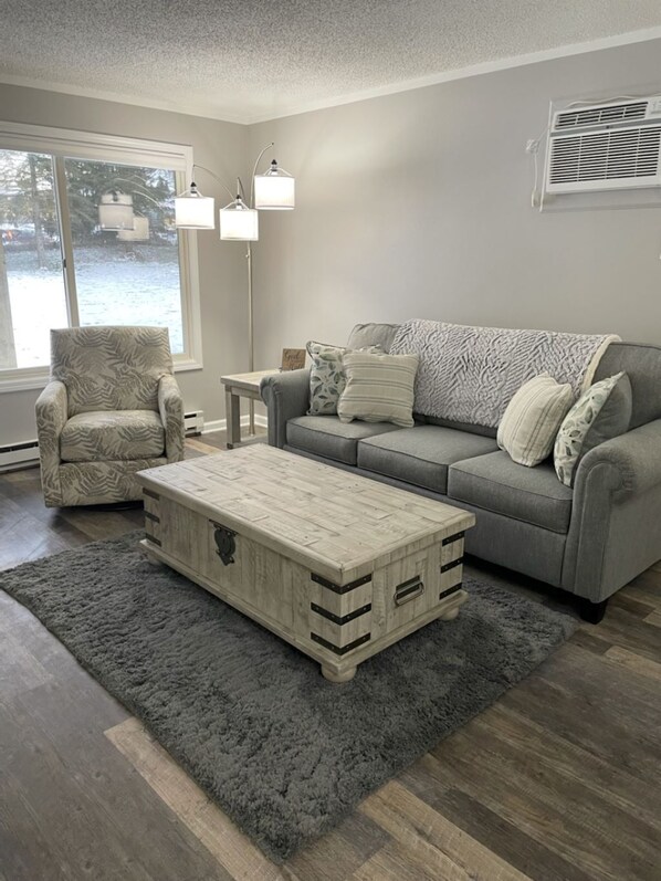 A living room with a grey sofa, a patterned armchair, a wooden coffee table, and a grey rug.