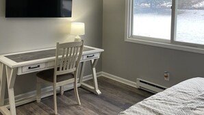 Ett sovrum med en säng, ett skrivbord med en stol, en tv som är monterad på väggen och ett fönster med utsikt över träd och snö.
