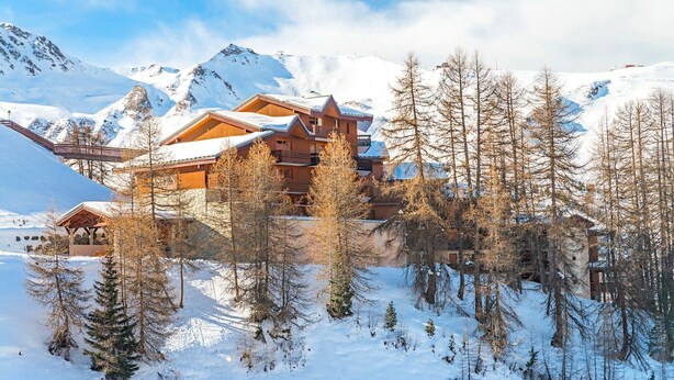 A wooden lodge with multiple balconies, surrounded by snow-covered mountains and trees. - travelski home select - Résidence Aspen 4* - 3 pièces 6/7 personnes (La Plagne)