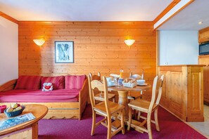 A cozy room with a wooden wall, a dining table with chairs, a sofa, and a small kitchen area.