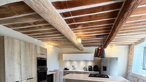 Een moderne keuken met houten kastjes, een centraal eiland met krukken, en zichtbare houten balken in het plafond.