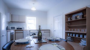 Een moderne keuken met witte kasten, een magnetron, een wasmachine en een eethoek met een houten tafel gedekt voor twee personen.