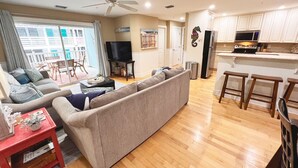 A living room with a sofa, a TV, a kitchen area with a microwave, and a dining area with stools. - Tybee Retreat Unit 2 (Tybee Island)