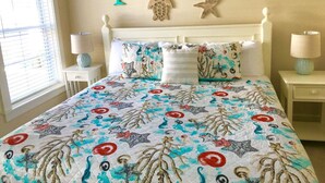 A bed with a floral and starfish patterned bedspread, a white headboard, and decorative wall art including shells and palm trees. - Tybee Retreat Unit 2 (Tybee Island)