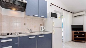Cozinha moderna com micro-ondas, chaleira e pia. Na área de estar adjacente, há uma TV e um móvel de entretenimento de madeira.